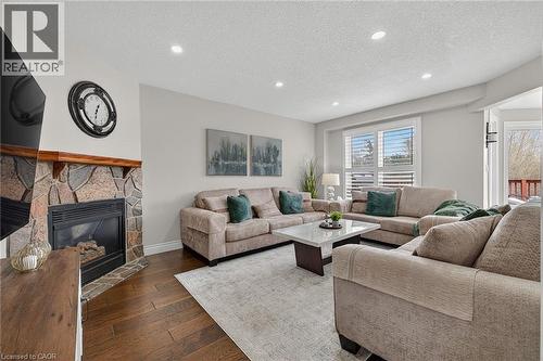 Living area featuring a stone-faced fireplace with a wood mantel, recessed lighting, wood-finish flooring, and white window shutters - 79 Holbrook Crescent, Cambridge, ON - Indoor Photo Showing Living Room With Fireplace