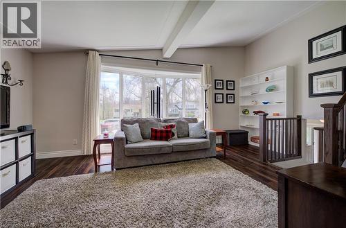 Living area featuring wood-finish flooring, a large bay window, a built-in white shelving unit, and dark wood stair railings - 172 Rennie Drive, Kitchener, ON - Indoor Photo Showing Living Room