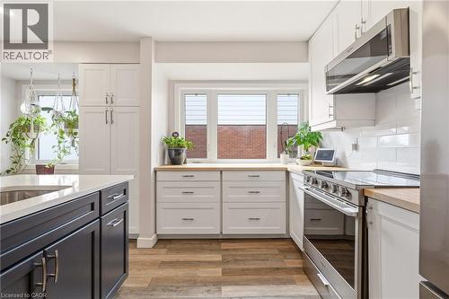 Modern kitchen featuring wood-finish flooring, white perimeter cabinetry with wood countertops, a stainless steel range and microwave, and a subway tile backsplash - 30 Darlington Drive, Hamilton, ON - Indoor Photo Showing Kitchen With Upgraded Kitchen