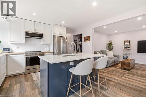 Contemporary kitchen featuring a navy island with a white countertop and seating, stainless steel appliances, white cabinetry, and wood-finish flooring - 30 Darlington Drive, Hamilton, ON - Indoor Photo Showing Kitchen With Upgraded Kitchen