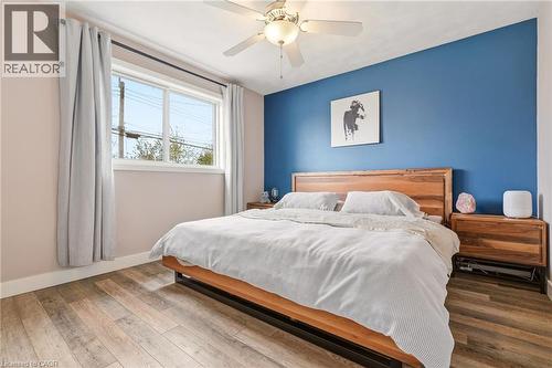 Room featuring a ceiling fan, wood-finish flooring, a window with a black rod, and a blue accent wall - 30 Darlington Drive, Hamilton, ON - Indoor Photo Showing Bedroom