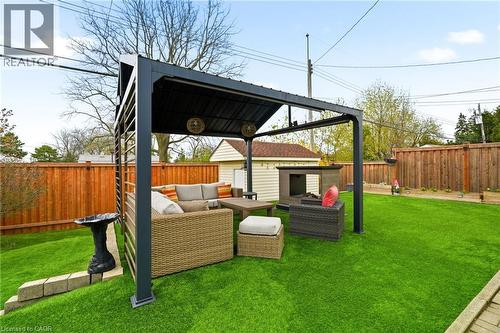 Expansive green turf backyard featuring a covered patio structure, full privacy fencing, a separate storage shed, and a built-in outdoor fireplace - 30 Darlington Drive, Hamilton, ON - Outdoor