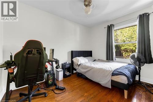 Hardwood-finish flooring throughout, featuring a single window with dark drapery, a ceiling fan with light fixture, and white wall finishes - 406 East 43Rd Street, Hamilton, ON - Indoor Photo Showing Bedroom