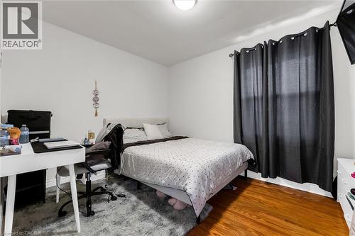 Bright interior space featuring wood-finish flooring, a window with black privacy drapes, and white walls - 406 East 43Rd Street, Hamilton, ON - Indoor Photo Showing Bedroom