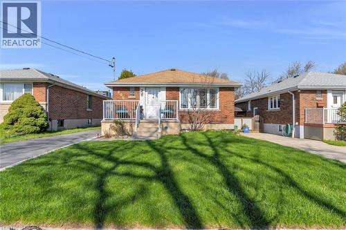 Brick facade residence with a light brown shingle roof, featuring a front porch with white railings and steps, multiple windows with white trim, and a concrete driveway - 406 East 43Rd Street, Hamilton, ON - Outdoor
