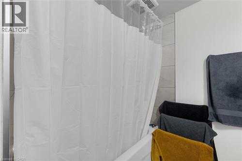 Bathtub with a white shower curtain, tiled shower surround, and a ceiling-mounted ventilation fan - 406 East 43Rd Street, Hamilton, ON - Indoor Photo Showing Bathroom