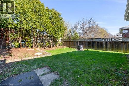 Grassed backyard featuring a wooden fence with lattice detailing, mature trees, and a concrete patio area - 406 East 43Rd Street, Hamilton, ON - Outdoor