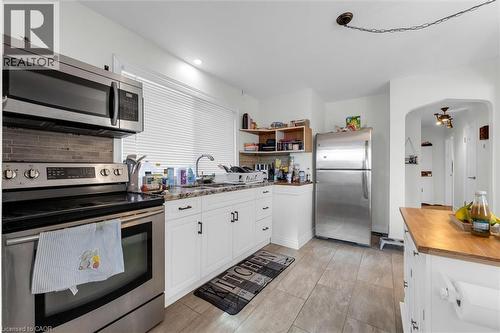 Modern kitchen with stainless steel appliances, white cabinetry, speckled countertops, and a tile backsplash - 406 East 43Rd Street, Hamilton, ON - Indoor Photo Showing Kitchen