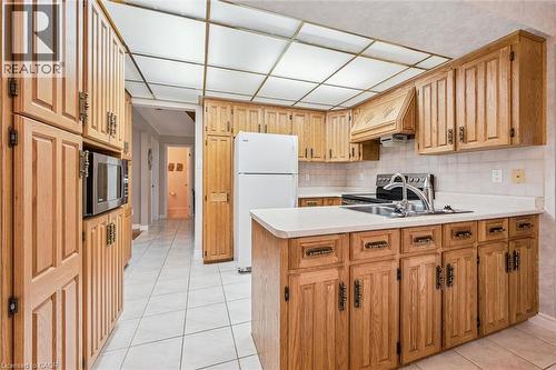 Bright kitchen featuring extensive wood-finish cabinetry, white tiled flooring, and a built-in microwave - 42 Trailview Drive, Kitchener, ON - Indoor Photo Showing Kitchen With Double Sink