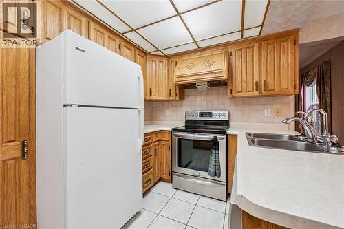 Kitchen featuring extensive wood cabinetry, white countertops, tile flooring, stainless steel range, and a double basin sink - 42 Trailview Drive, Kitchener, ON - Indoor Photo Showing Kitchen With Double Sink