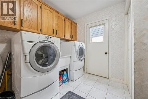 Laundry area featuring oak-finish cabinetry, a utility sink, and white ceramic tile flooring - 42 Trailview Drive, Kitchener, ON - Indoor Photo Showing Laundry Room