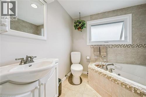 Bathroom featuring a built-in tub with tile surround and mosaic accent, a white pedestal sink with vanity, a commode, and a frosted window - 42 Trailview Drive, Kitchener, ON - Indoor Photo Showing Bathroom