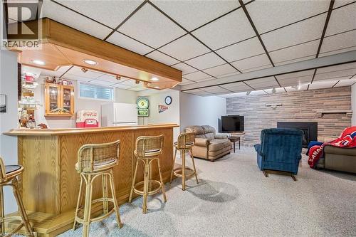 Finished lower level featuring a built-in wood-finish bar with integrated recessed lighting, a stone-accented wall, a fireplace with a mantel, and light-colored carpeting - 42 Trailview Drive, Kitchener, ON - Indoor Photo Showing Other Room