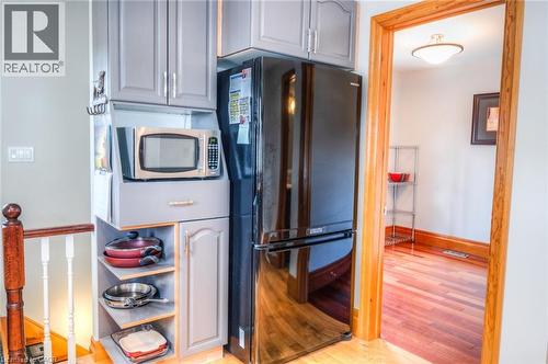 Integrated kitchen cabinetry featuring an overhead microwave niche, open shelving, a black refrigerator, and a lower storage cabinet - 46 2 Avenue, Kitchener, ON - Indoor