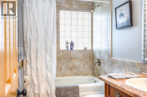 Full bathroom featuring a tub/shower combination with tile surround, a glass block window, and a vanity with an integrated sink and wood-finish cabinetry - 46 2 Avenue, Kitchener, ON - Indoor Photo Showing Bathroom