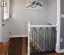 Entryway featuring wood-finish flooring, white paneled door with glass insert, white baseboards, and a staircase with white newel posts and black wrought iron balusters - 