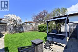 Private fenced backyard featuring a manicured lawn, paved patio, and a covered outdoor cooking station - 