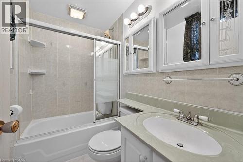 Bathroom featuring a white bathtub with sliding glass doors, light-toned tiled shower surround, a vanity with an integrated sink, and white framed medicine cabinets - 192 Ivon Avenue, Hamilton, ON - Indoor Photo Showing Bathroom