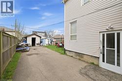 Paved driveway extending to a detached shed, bordered by a wooden privacy fence and a vinyl-sided exterior wall with a glass-paneled entry door - 