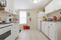 Kitchen featuring white cabinetry, light-toned tiled flooring, and a window with horizontal blinds - 