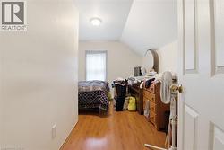 Room featuring wood-finish flooring, a single window, a sloped ceiling, a flush mount light fixture, and a paneled interior door - 