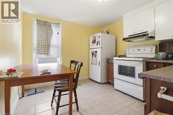 Kitchen featuring light yellow walls, white upper cabinetry, brown lower cabinetry, and light-toned tile flooring - 