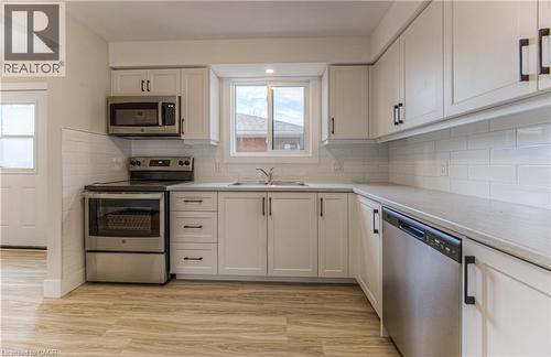 Kitchen featuring white shaker-style cabinetry, stainless steel appliances, light-toned countertops, white subway tile backsplash, and wood-finish flooring - 40 Daniel Avenue Unit# 2, Kitchener, ON - Indoor Photo Showing Kitchen With Stainless Steel Kitchen With Double Sink