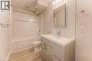 Bathroom featuring a white subway tile backsplash, a single vanity with a white countertop and gray cabinetry, a white bathtub with a shower kit, and wood-finish flooring - 40 Daniel Avenue Unit# 2, Kitchener, ON  - Indoor Photo Showing Bathroom 