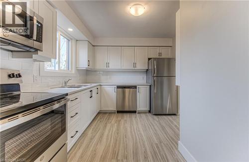Modern kitchen featuring white shaker cabinetry, stainless steel appliances, wood-finish flooring, white subway tile backsplash, and a double basin sink - 40 Daniel Avenue Unit# 2, Kitchener, ON - Indoor Photo Showing Kitchen With Stainless Steel Kitchen
