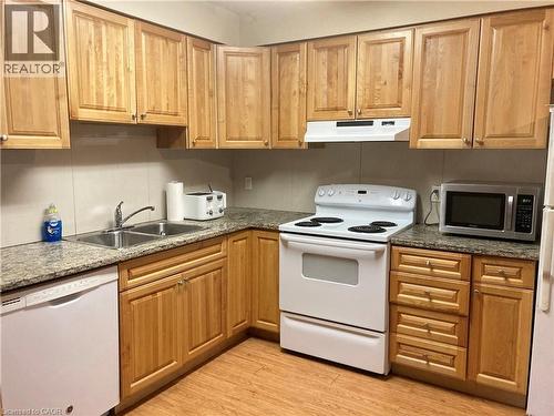 Kitchen featuring wood-finish cabinetry, speckled countertops, a double basin stainless steel sink, a white electric range, and wood-finish flooring - 392 Albert Street Unit# 302, Waterloo, ON - Indoor Photo Showing Kitchen With Double Sink