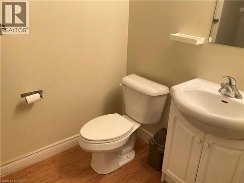 Bathroom featuring a white toilet, pedestal sink with cabinet storage, and wood-finish flooring - 392 Albert Street Unit# 302, Waterloo, ON - Indoor Photo Showing Bathroom