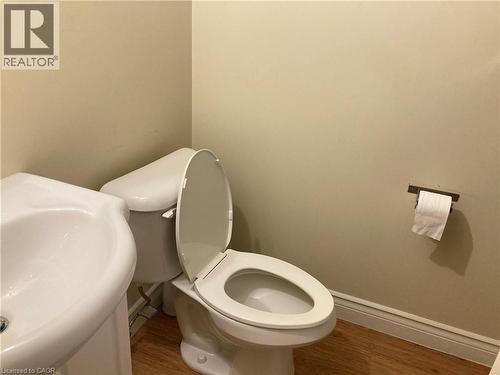 Compact powder room featuring a white porcelain pedestal sink, white toilet, and wood-finish flooring - 392 Albert Street Unit# 302, Waterloo, ON - Indoor Photo Showing Bathroom