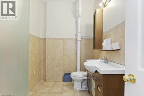 Bathroom featuring tile flooring, half-tiled walls with decorative trim, a wood-finish vanity with an integrated sink, a wall-mounted wood-finish medicine cabinet, and a wall-mounted light fixture - 238-242 King Street E, Hamilton, ON 
