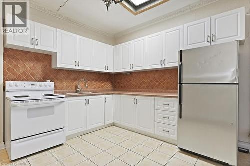 Kitchen featuring white cabinetry, a white electric range, a stainless steel refrigerator, a tiled backsplash, and light-toned flooring - 238-242 King Street E, Hamilton, ON 