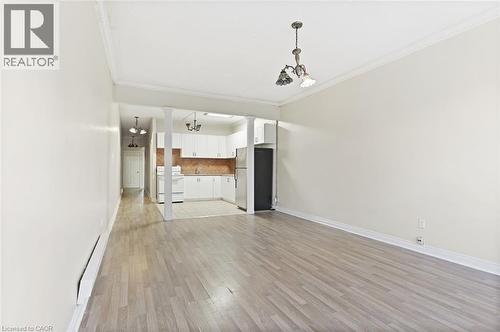 Spacious living area featuring wood-finish flooring, crown molding, and a kitchen with white cabinetry and a tiled backsplash - 238-242 King Street E, Hamilton, ON 