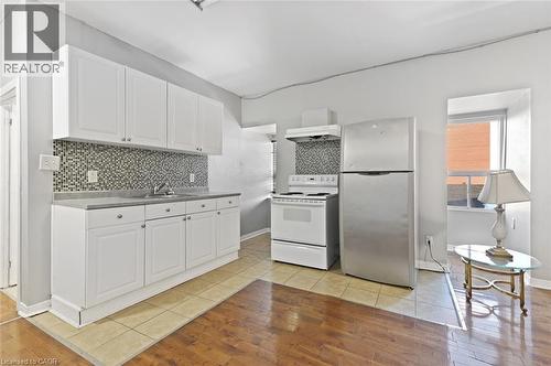 Kitchen area featuring white cabinetry, a mosaic tile backsplash, a stainless steel refrigerator, and a white electric range with an overhead vent - 238-242 King Street E, Hamilton, ON 