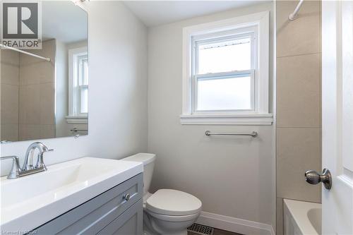 Bathroom featuring a single window, a light gray vanity with a white countertop and integrated sink, chrome faucet fixtures, a toilet, and light-colored tile surrounding the tub - 2337 Barclay Road, Burlington, ON - Indoor Photo Showing Bathroom
