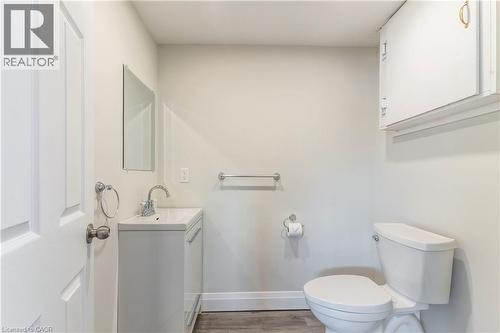 Bathroom featuring a white vanity with integrated sink, chrome faucet, wall-mounted mirror, and wood-finish flooring - 2337 Barclay Road, Burlington, ON - Indoor Photo Showing Bathroom