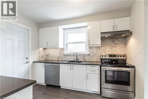 Kitchen featuring white cabinetry, dark countertops, a tile backsplash, stainless steel appliances, and wood-finish flooring - 2337 Barclay Road, Burlington, ON - Indoor Photo Showing Kitchen With Stainless Steel Kitchen With Double Sink With Upgraded Kitchen