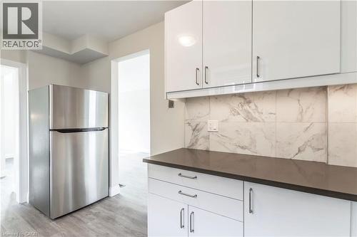 Kitchen featuring a stainless steel refrigerator, white gloss cabinetry, dark countertops, and a white and grey patterned tile backsplash - 2337 Barclay Road, Burlington, ON - Indoor Photo Showing Kitchen