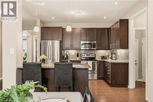 Kitchen featuring dark wood cabinetry, stainless steel appliances, speckled countertops, a tile backsplash, and an island with pendant lighting - 42 Yager Drive, Binbrook, ON - Indoor Photo Showing Kitchen With Stainless Steel Kitchen With Upgraded Kitchen
