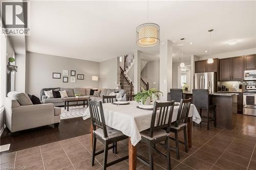 Open-concept living space featuring a dining area with a contemporary chandelier, a kitchen with dark wood-finish cabinetry and stainless steel appliances, and a living room with wood-finish flooring - 42 Yager Drive, Binbrook, ON - Indoor Photo Showing Other Room