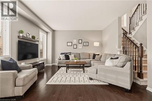 Spacious living area featuring dark wood-finish flooring, a contemporary staircase with dark wood banister and balusters, and multiple windows with blinds - 42 Yager Drive, Binbrook, ON - Indoor Photo Showing Living Room