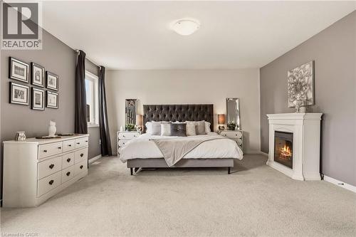 Spacious room featuring light-toned carpeting, a corner fireplace with a white mantel, and a window with dark drapery - 42 Yager Drive, Binbrook, ON - Indoor Photo Showing Bedroom