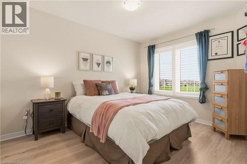 Neutral paint palette throughout, featuring wood-finish flooring, a window with plantation shutters, and a ceiling-mounted light fixture - 42 Yager Drive, Binbrook, ON - Indoor Photo Showing Bedroom