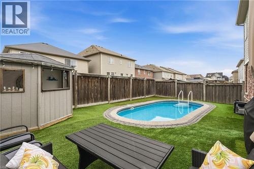 Backyard featuring an oval swimming pool with perimeter paver surround, artificial turf, wood privacy fencing, and a built-in outdoor cabana bar - 42 Yager Drive, Binbrook, ON - Outdoor With Backyard