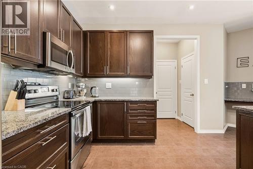 Kitchen featuring dark wood-finish cabinetry, light-toned granite countertops, a subway tile backsplash, and stainless steel appliances including a range and microwave - 42 Yager Drive, Binbrook, ON - Indoor Photo Showing Kitchen