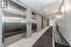 Lobby area featuring two brushed stainless steel elevators, light gray walls, white tiled flooring, and recessed ceiling lighting - 