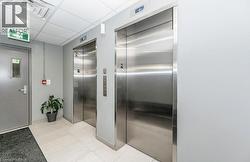 Dual stainless steel elevators in a common area featuring light gray walls, white floor tiling, and a dropped ceiling with recessed lighting - 