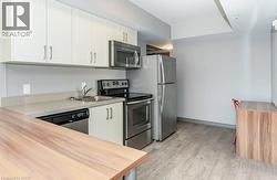 Modern kitchen featuring light cabinetry, stainless steel appliances, light-toned countertops, and wood-finish flooring - 